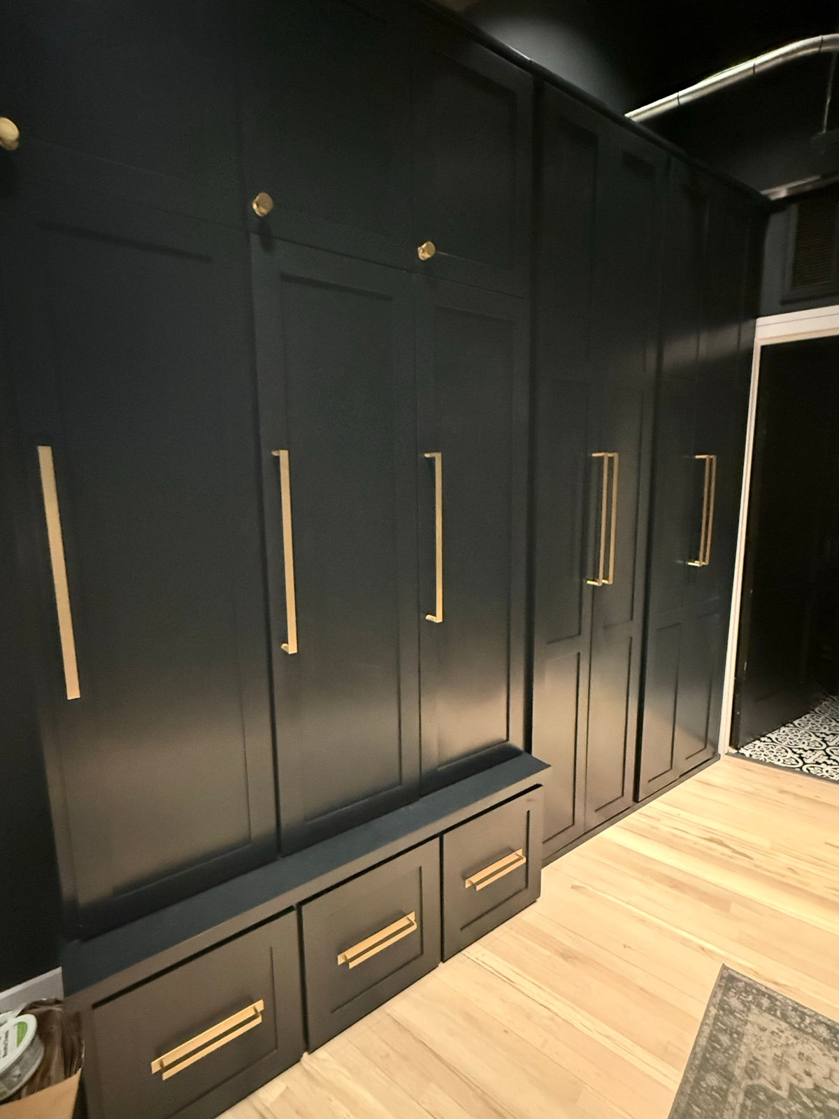 Floor to ceiling black lockers with brass pulls and a bench