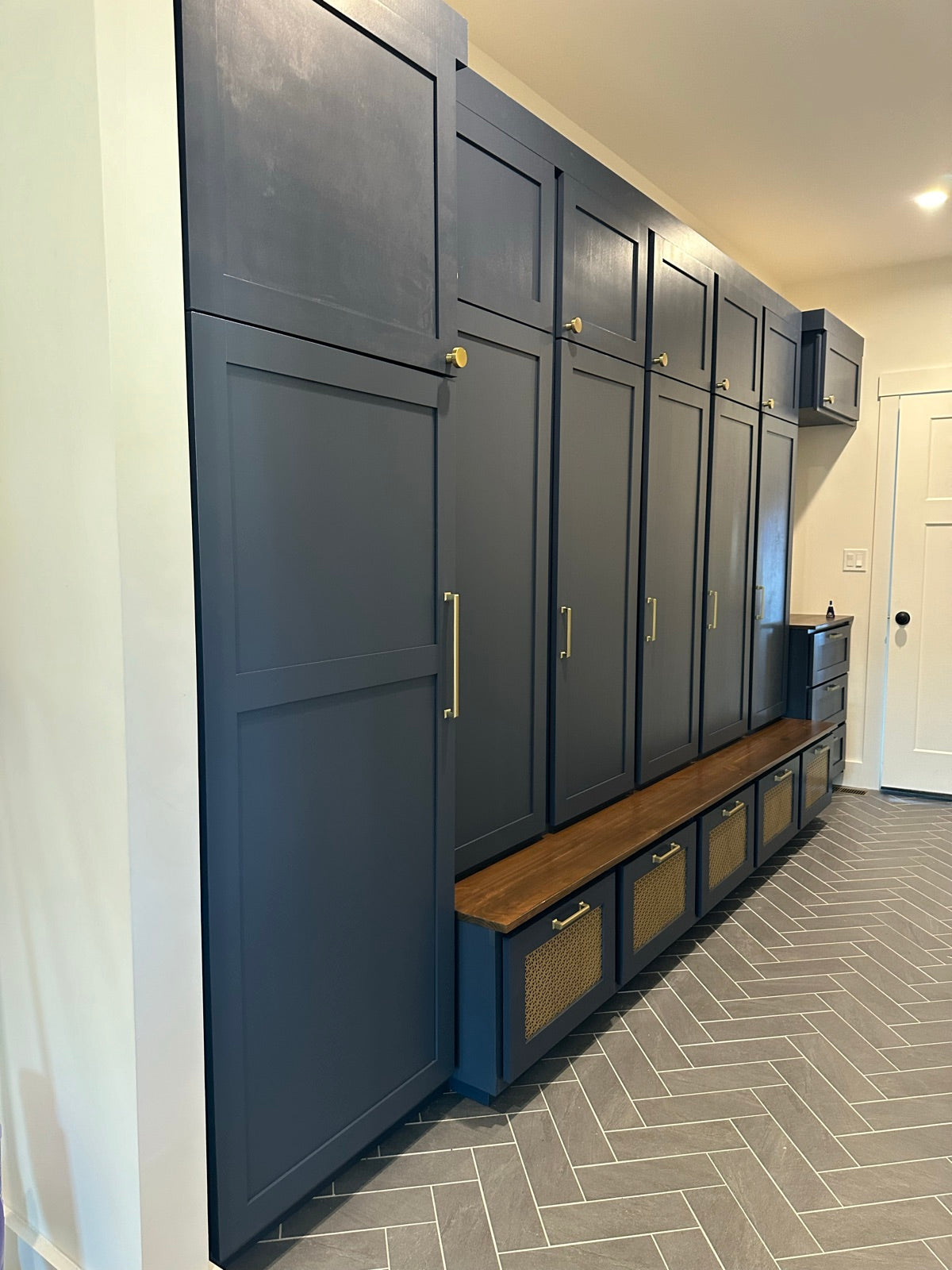 Full wall navy mudroom with cane front drawers and a wood bench top